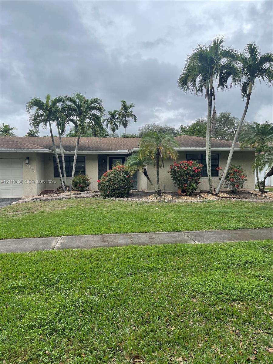 Single-story exterior featuring a stucco facade, attached garage, manicured lawn, stone landscaping beds, and mature palm trees