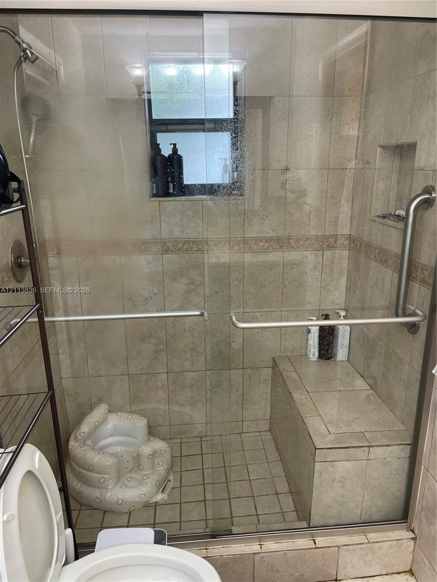 Walk-in shower enclosure featuring floor-to-ceiling tile, a built-in bench seat, a recessed wall niche, and a glass sliding door