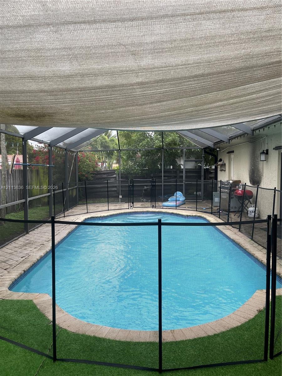 Screen-enclosed swimming pool featuring a paved perimeter, removable safety fencing, and an overhead shade canopy