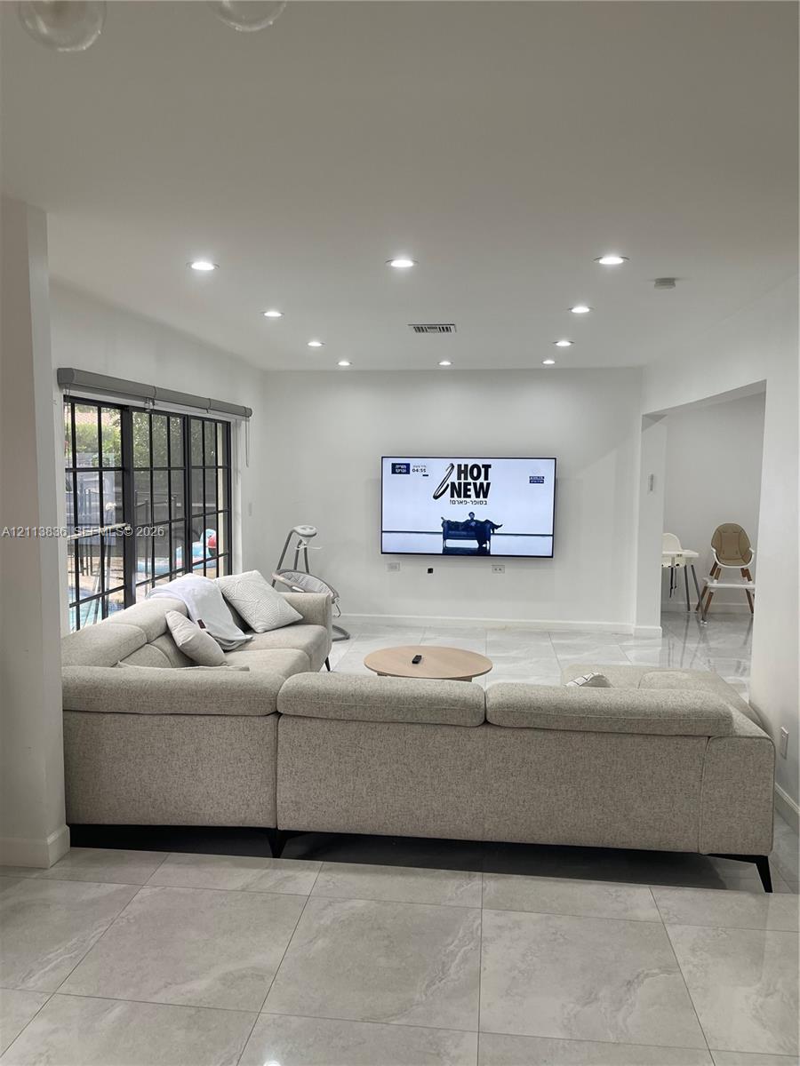 Open-concept living space featuring large-format tile flooring, recessed lighting, and expansive floor-to-ceiling windows with dark mullions