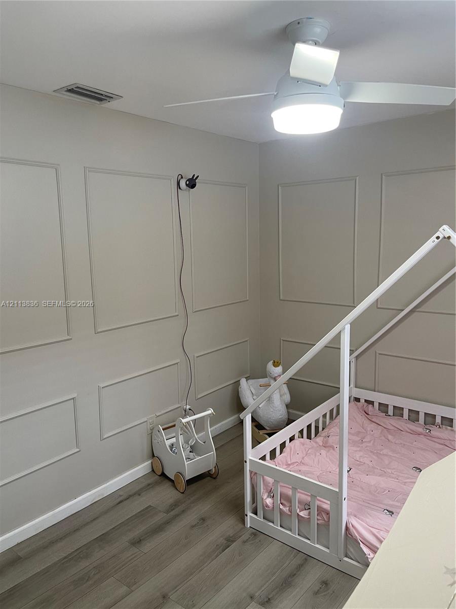 Room featuring neutral-toned wall molding, wood-finish flooring, and a ceiling-mounted fan with integrated lighting