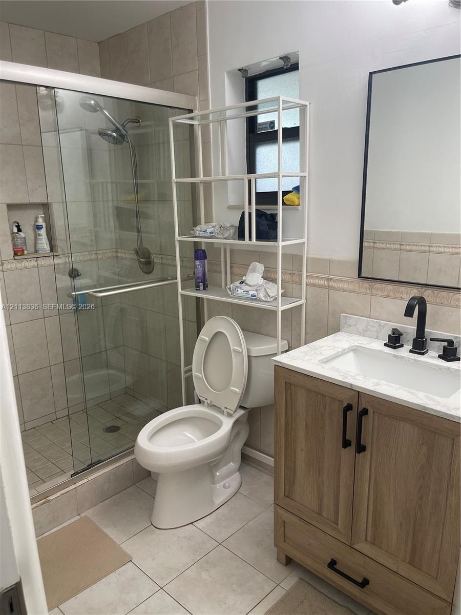 Bathroom featuring a wood-finish vanity with a stone-top integrated sink, matte black hardware, a glass-enclosed shower with tiled walls and a recessed niche, and a wall-mounted rectangular mirror with a black frame