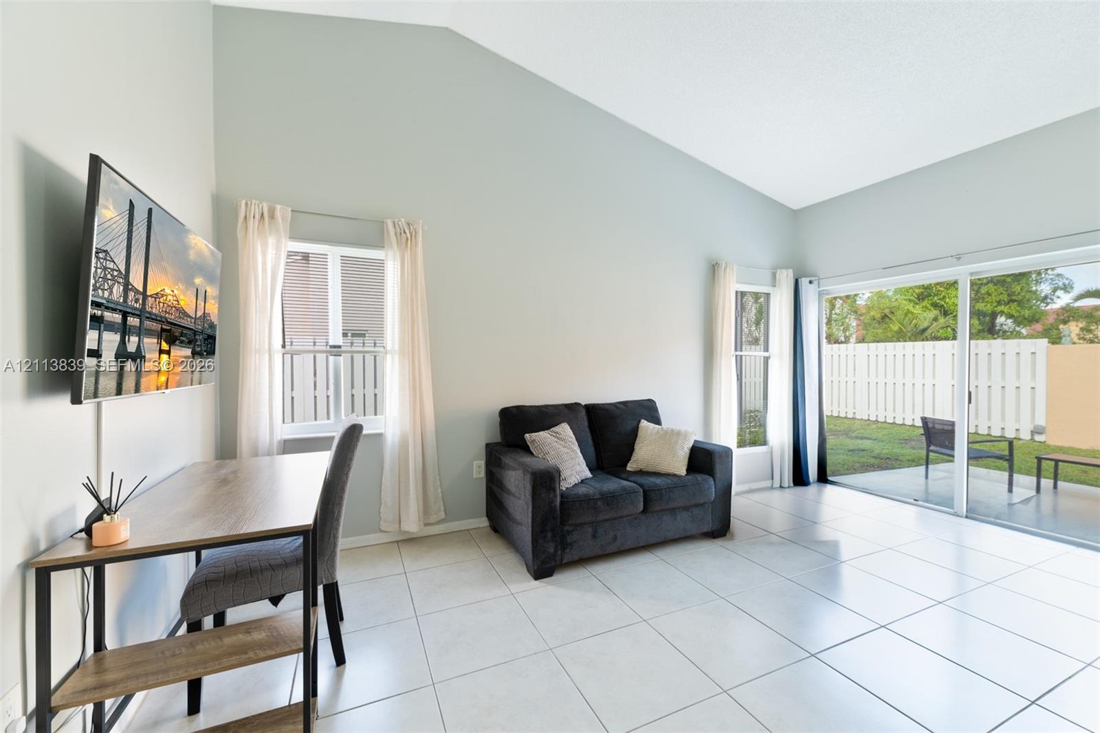 Living area featuring vaulted ceilings, large-format tile flooring, and sliding glass doors providing access to a concrete patio