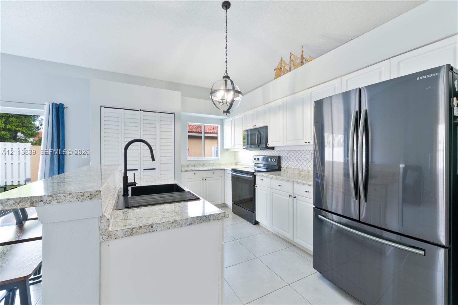 Kitchen featuring white cabinetry, stone-finish countertops, stainless steel appliances, a matte black faucet, and an overhead pendant light fixture