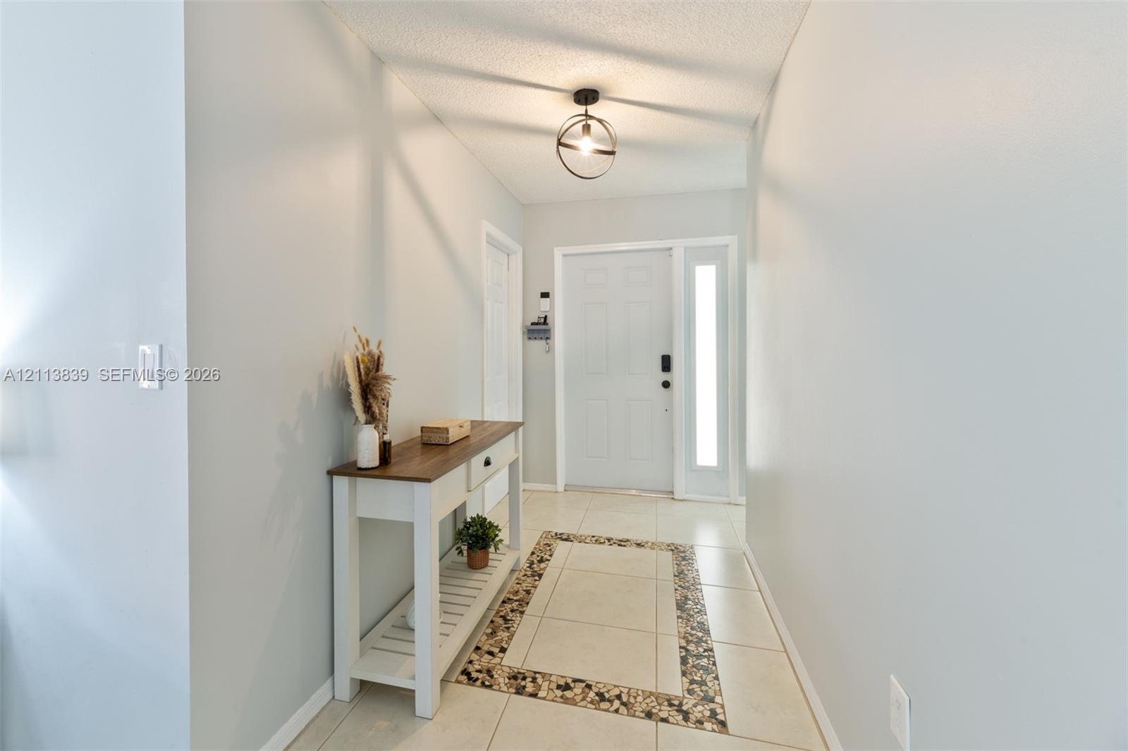 Entryway featuring tile flooring with decorative stone-tiled inlay, six-panel exterior door with sidelight, and matte black spherical pendant lighting