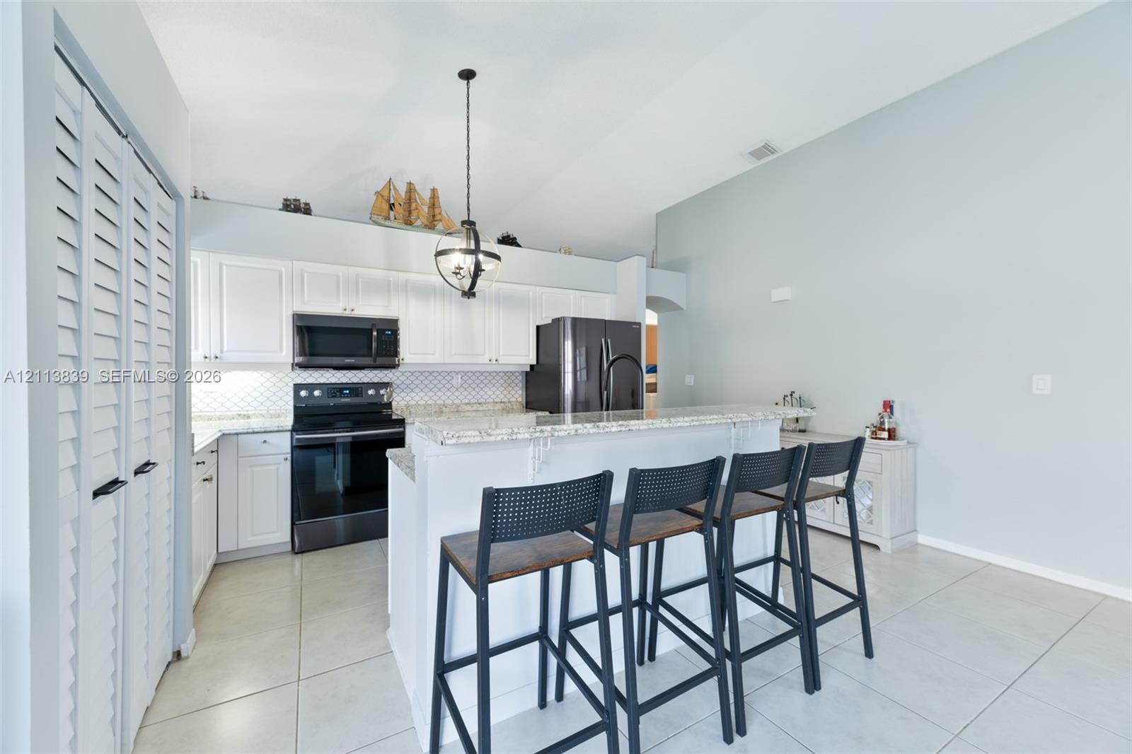 Kitchen featuring white cabinetry, stone-surface countertops, a geometric-pattern backsplash, dark-finish appliances, and a vaulted ceiling with a pendant light fixture