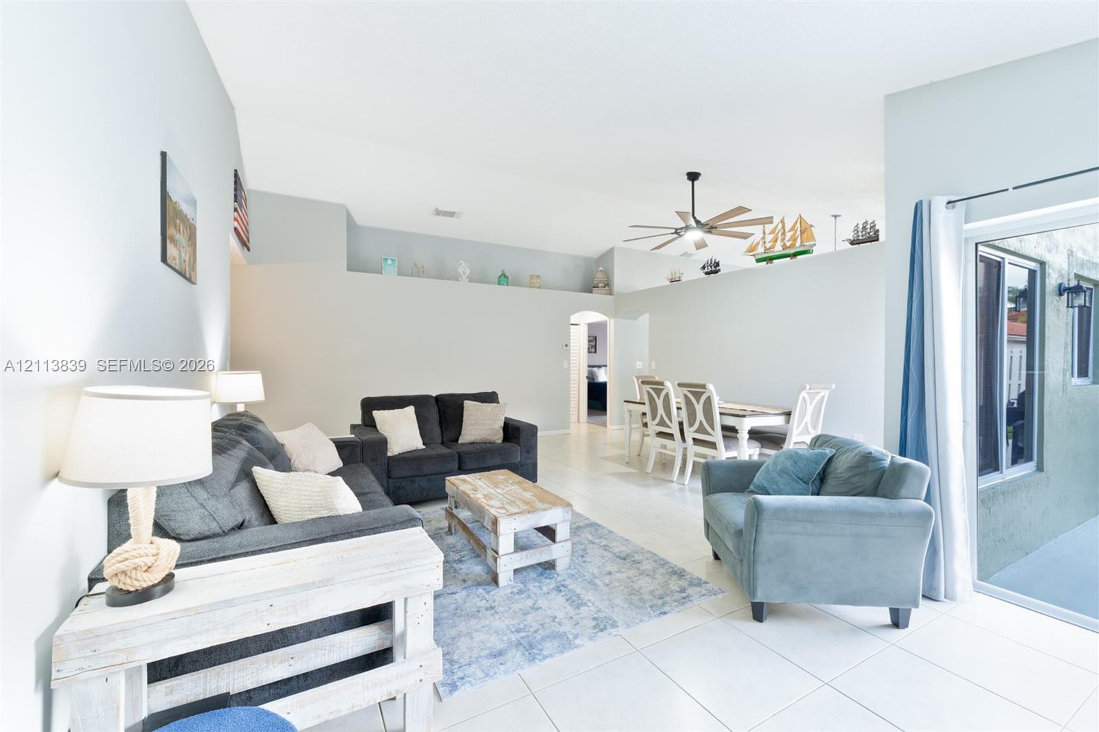 High-ceiling living area with large-format tile flooring, built-in display ledge, and sliding glass door access to the exterior