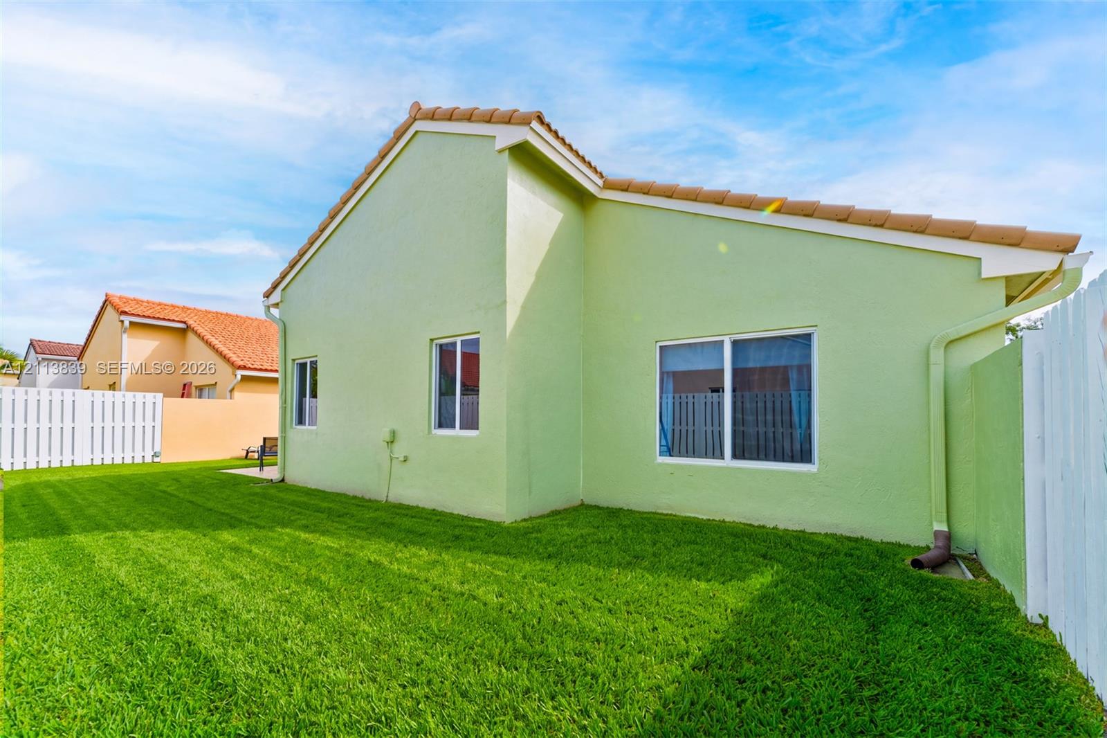 Stucco exterior home featuring a terracotta-tiled roof, white-framed sliding windows, and a private fenced yard with lawn