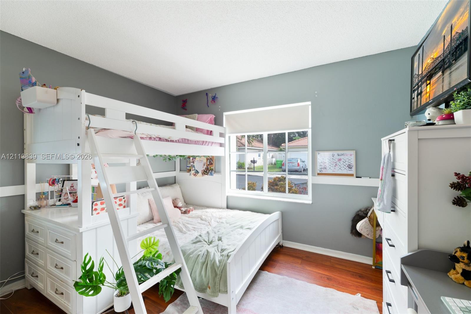 Bedroom featuring wood-finish flooring, a multi-pane window with a roller shade, and horizontal wall trim