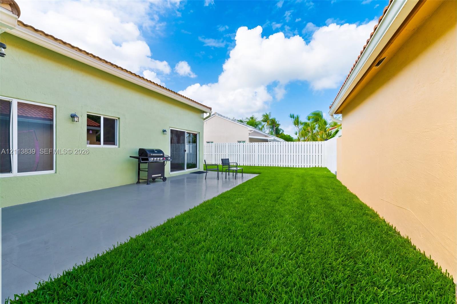 Private backyard featuring a poured concrete patio, manicured lawn, and white privacy fencing