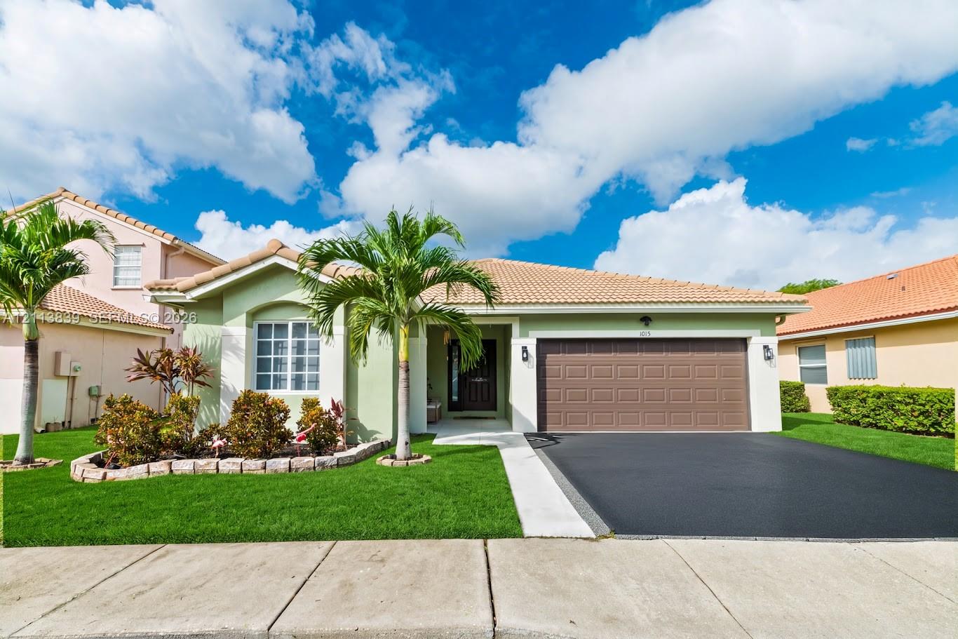 Single-story exterior featuring a tile roof, stucco siding, a multi-pane window with stone-finish edging, and a paved driveway leading to a two-car garage