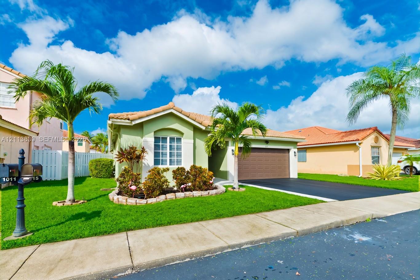 Single-story stucco exterior featuring a tile roof, two-car garage, manicured lawn, and stone-bordered landscaping beds