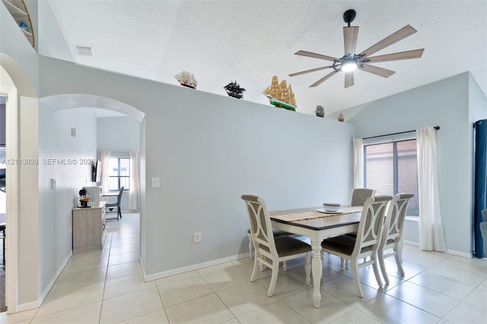 Vaulted ceilings, large-format tile flooring, arched architectural detail, multi-blade ceiling fan with integrated lighting, and sliding glass door