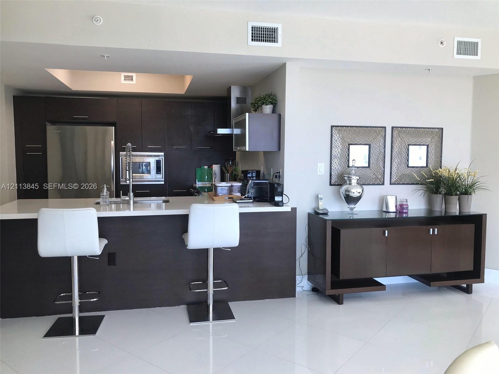 Kitchen featuring dark wood-finish cabinetry, white solid-surface countertops, integrated stainless steel appliances, and tile flooring