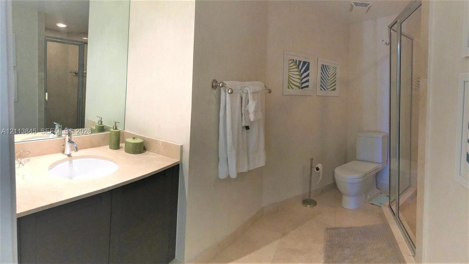 Bathroom featuring a vanity with a stone countertop, an integrated sink with a chrome faucet, full-width mirror, tile flooring, and a glass-enclosed shower