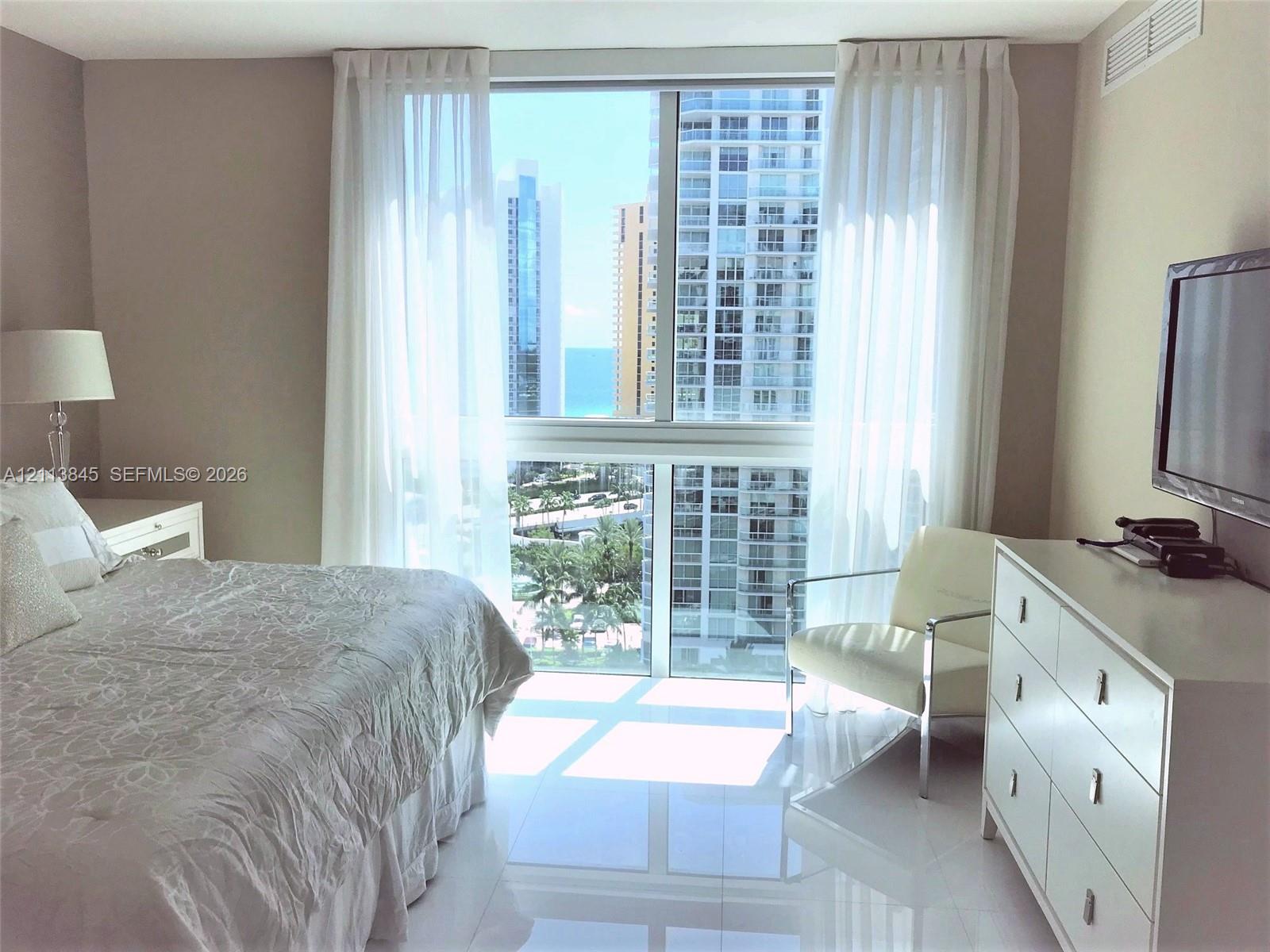 Floor-to-ceiling windows featuring urban and ocean scenery, high-gloss tile flooring, and neutral wall tones Floor-to-ceiling windows featuring urban and ocean scenery, high-gloss tile flooring, and neutral wall tones
