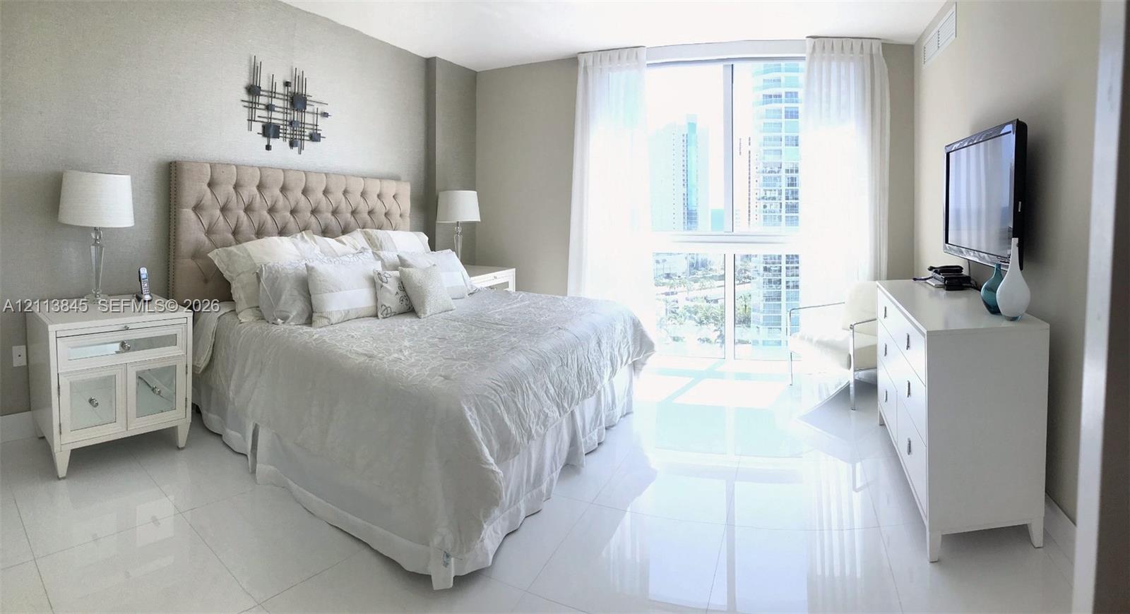 Floor-to-ceiling windows featuring urban scenery, complemented by polished light-toned tile flooring throughout Floor-to-ceiling windows featuring urban scenery, complemented by polished light-toned tile flooring throughout