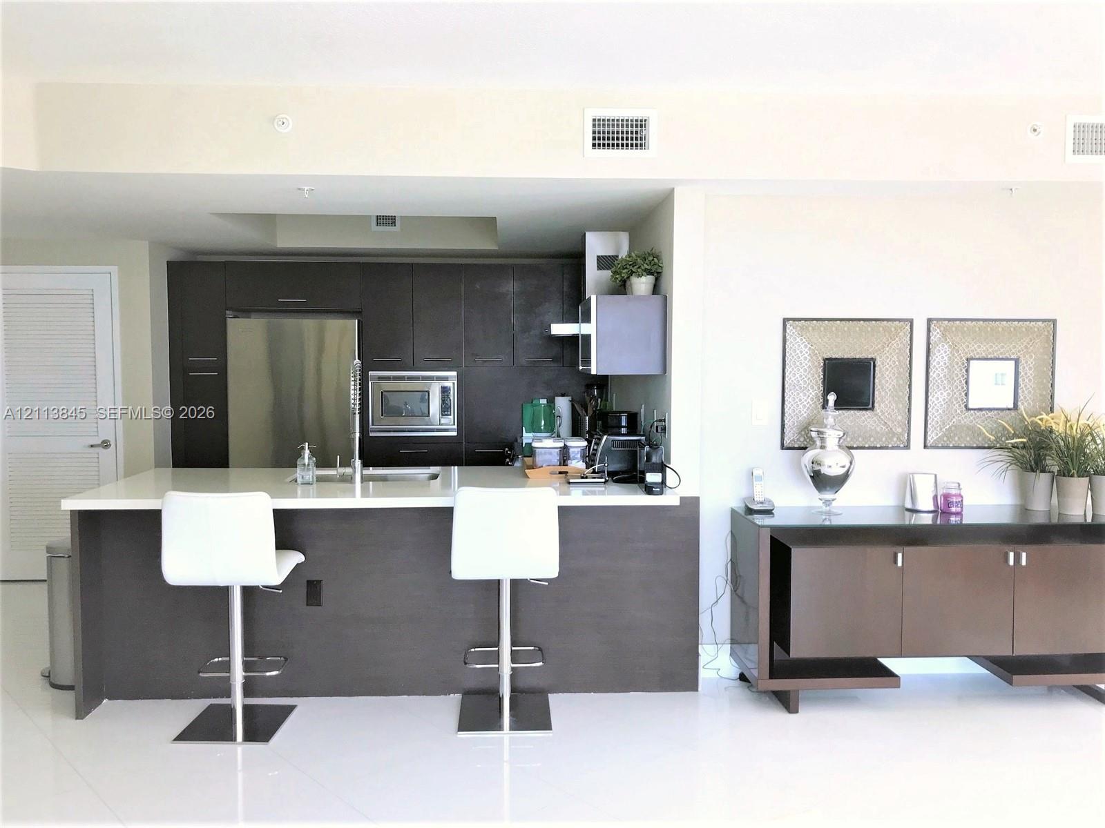 Kitchen featuring flat-panel dark wood cabinetry, a breakfast bar with stone-surface countertop, stainless steel appliances, and high-gloss flooring