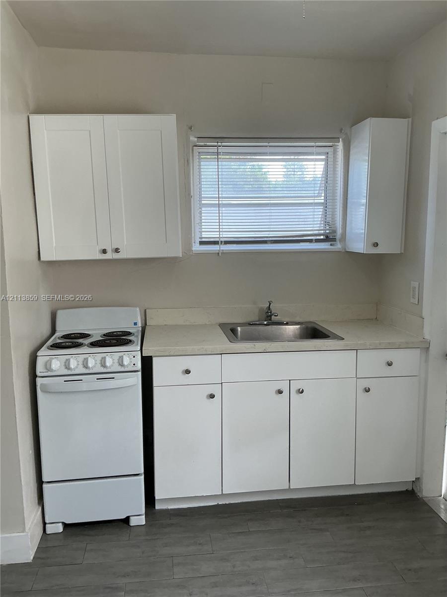 Kitchen area featuring white cabinetry, a neutral-toned countertop, an integrated stainless steel sink, a freestanding electric range, and wood-finish flooring