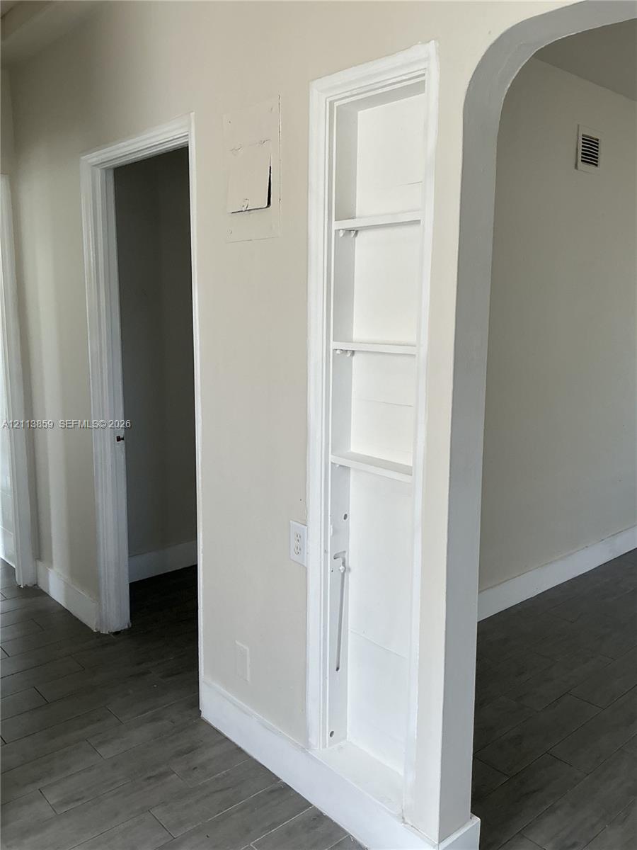 Built-in wall shelving, arched doorway, and wood-finish flooring