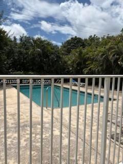 In-ground swimming pool featuring a metal safety fence, concrete decking, and mature perimeter trees