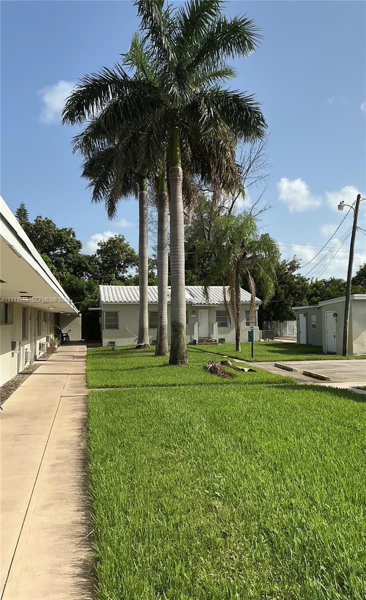 Exterior grounds featuring mature palm trees, a concrete walkway, and a manicured lawn