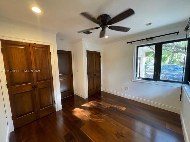 Interior space featuring wood-finish flooring, stained wood double-door closet cabinetry, a multi-pane window with a black frame, and a ceiling-mounted fan