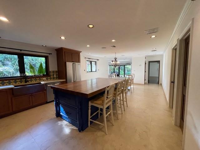 Kitchen featuring an expansive center island with a wood countertop, custom cabinetry, farmhouse sink, stone-finish tile flooring, and recessed lighting