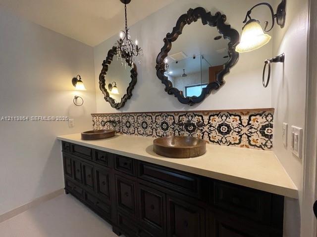 Double vanity featuring dark wood cabinetry, a solid surface countertop, dual vessel sinks, decorative patterned tile backsplash, and ornate wall-mounted mirrors