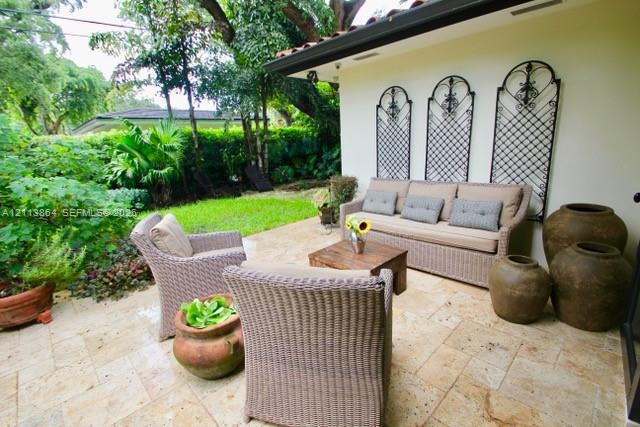 Covered patio featuring stone-tile flooring, decorative metal wall grilles, and landscaping