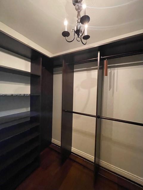 Custom storage system featuring dark wood-finish shelving and hanging rods, wood-finish flooring, and a traditional multi-arm chandelier