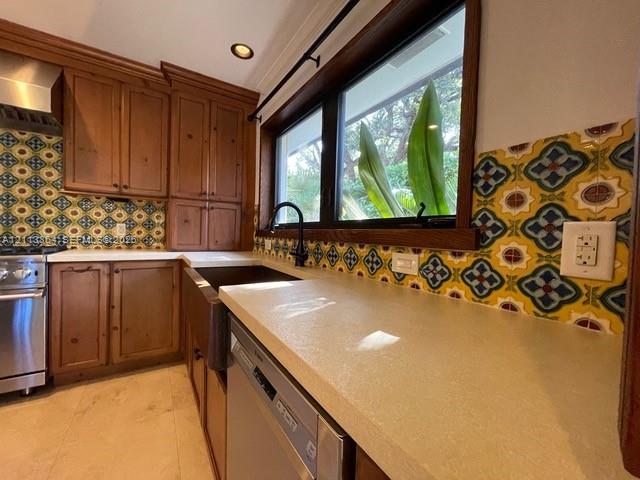 Kitchen featuring custom wood cabinetry, patterned tile backsplash, solid-surface countertops, farmhouse sink with matte black hardware, and stainless steel dishwasher