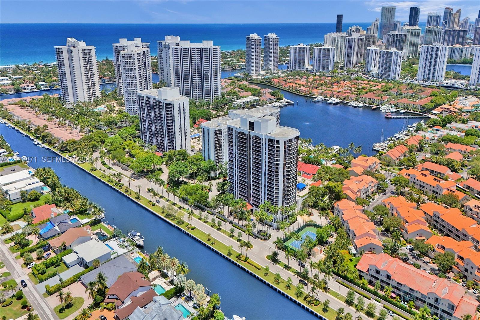 Aerial perspective of coastal high-rise building featuring proximity to deep-water canals, on-site tennis court, and expansive ocean and city skyline horizon Aerial perspective of coastal high-rise building featuring proximity to deep-water canals, on-site tennis court, and expansive ocean and city skyline horizon
