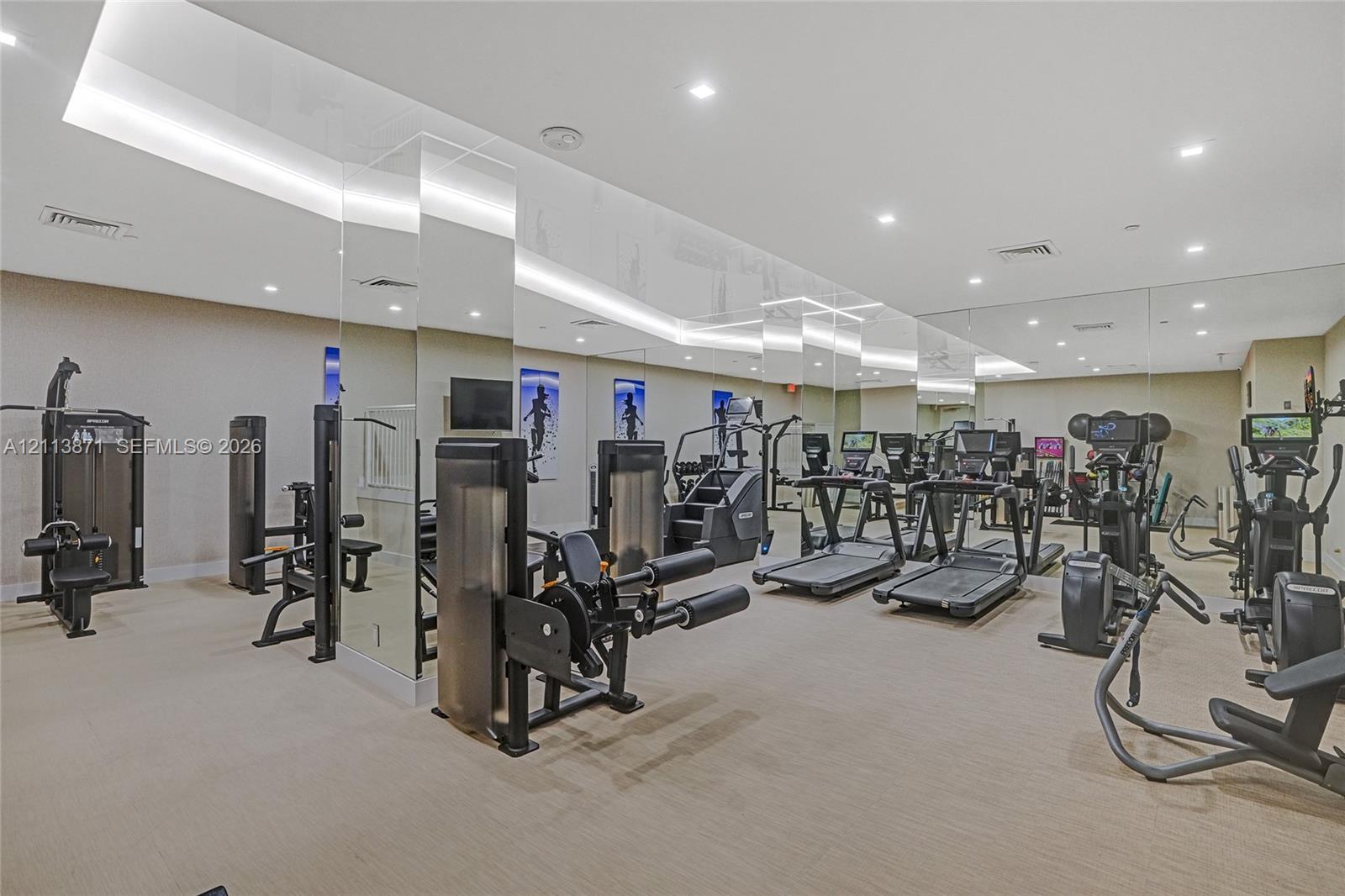 Fitness center featuring mirrored walls, recessed ceiling lighting, and neutral wall-to-wall carpeting Fitness center featuring mirrored walls, recessed ceiling lighting, and neutral wall-to-wall carpeting