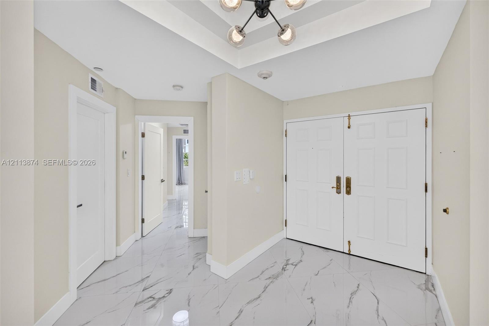 Foyer featuring large-format stone-look tile flooring, a tray ceiling, and a multi-arm pendant light fixture