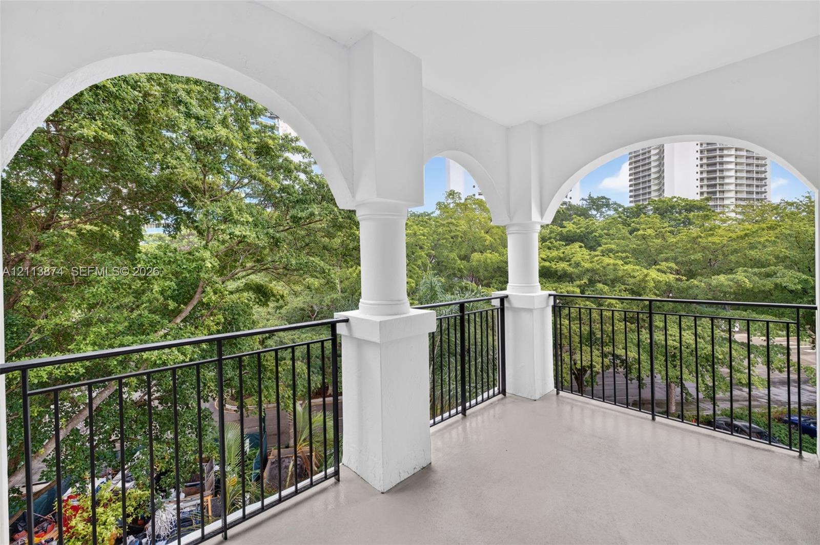 Covered balcony featuring arched architectural openings, substantial pillars, and a black metal railing