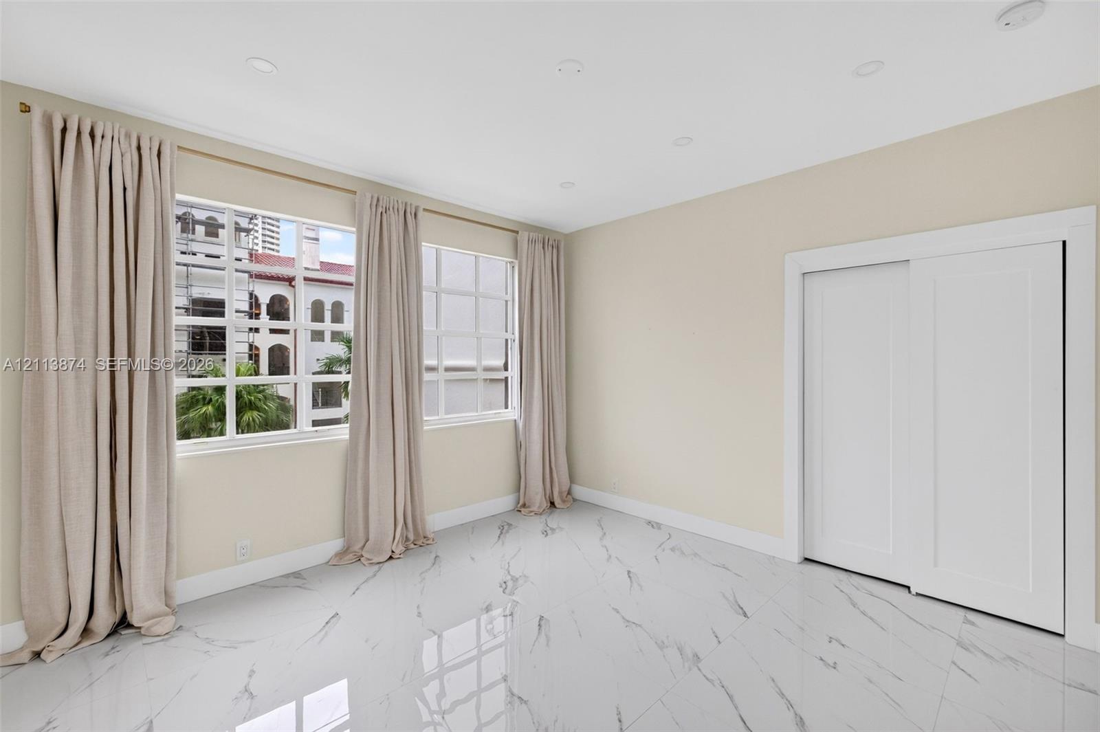 Polished stone-look tile flooring, grid-patterned windows, and a built-in sliding-door closet, illuminated by recessed lighting
