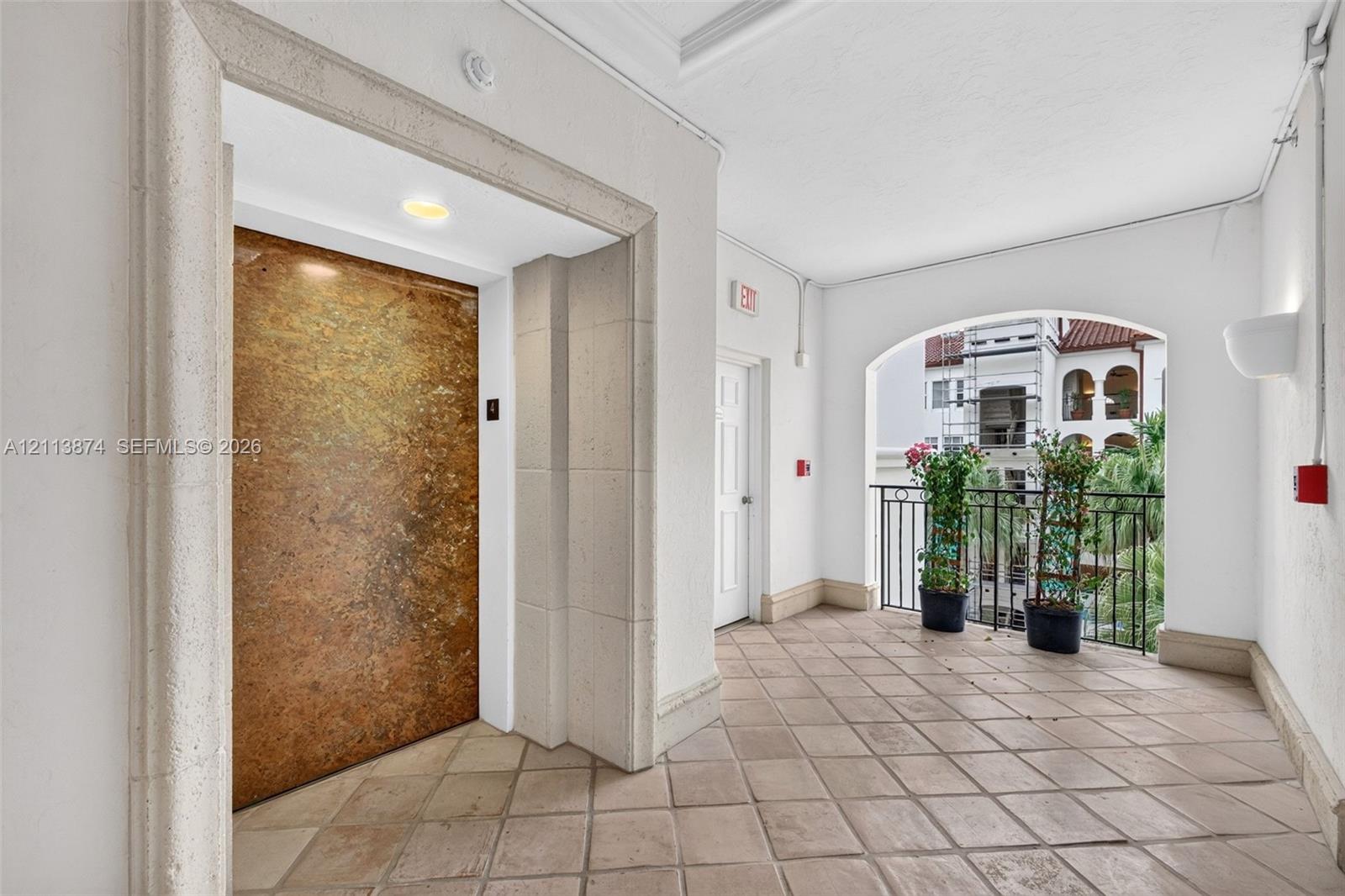 Elevator lobby featuring metallic finish elevator doors, stone-tiled flooring, arched masonry detailing, and a black wrought-iron railing