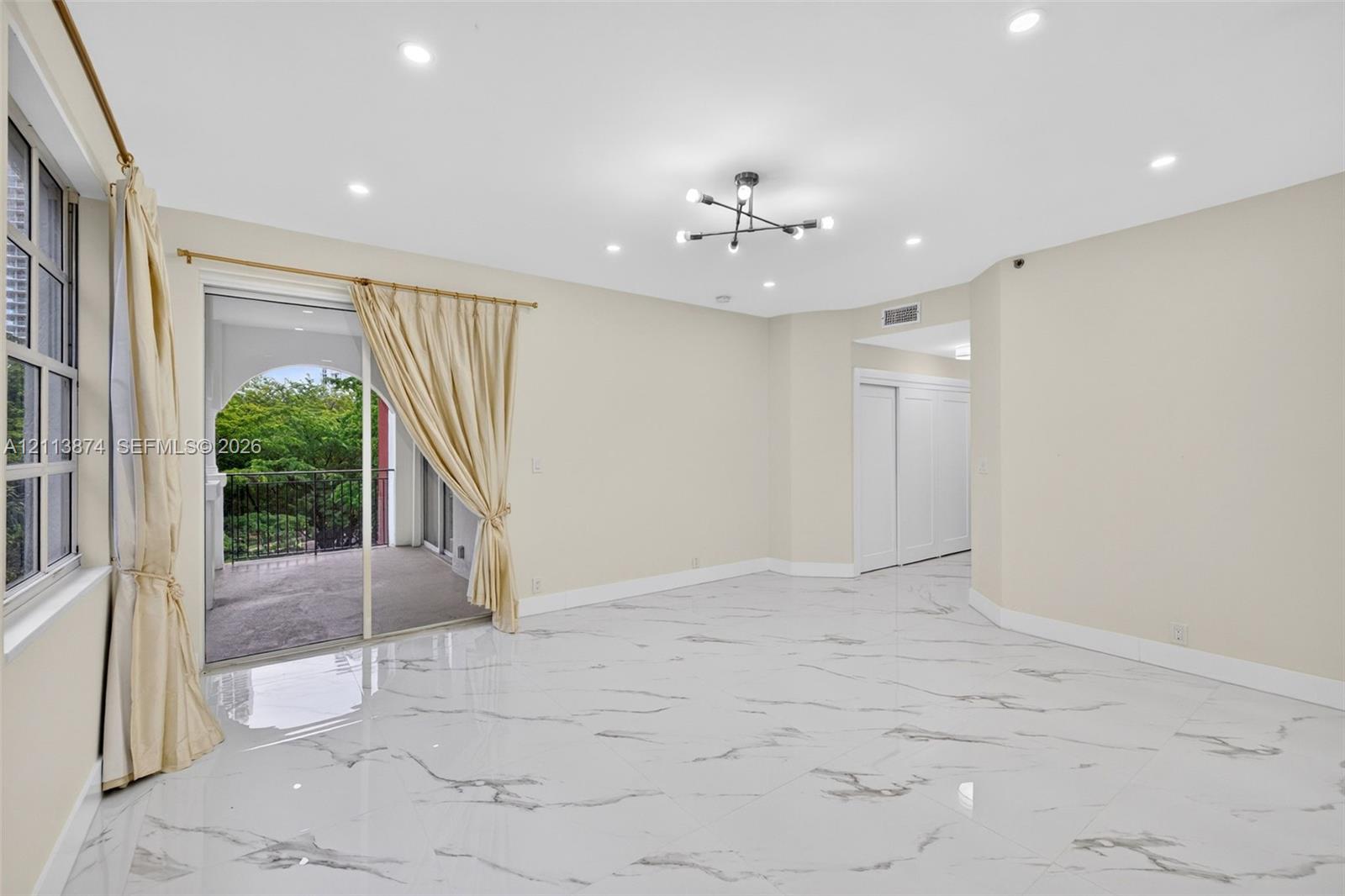 Large format stone-finish tile flooring, multi-arm geometric ceiling light fixture, recessed lighting, sliding glass door, and covered balcony with metal railing