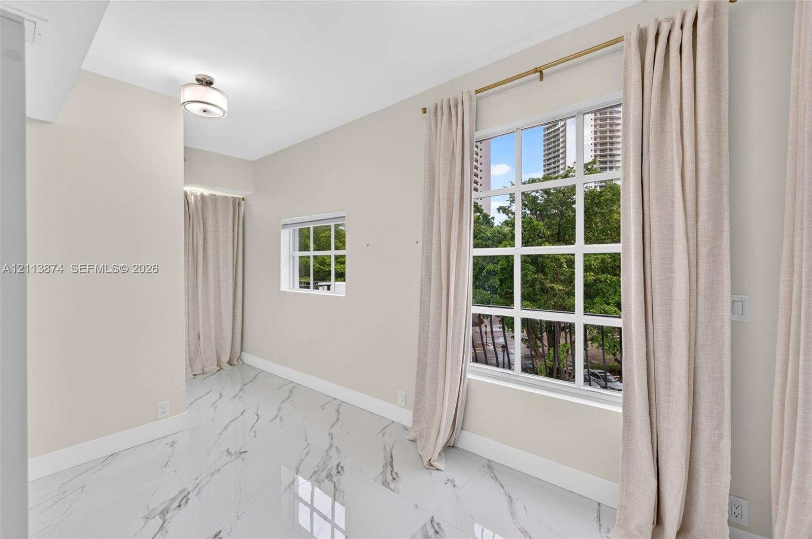 Large-format tile flooring with marble-style veining, multiple multi-pane windows, and a flush-mount drum ceiling light fixture