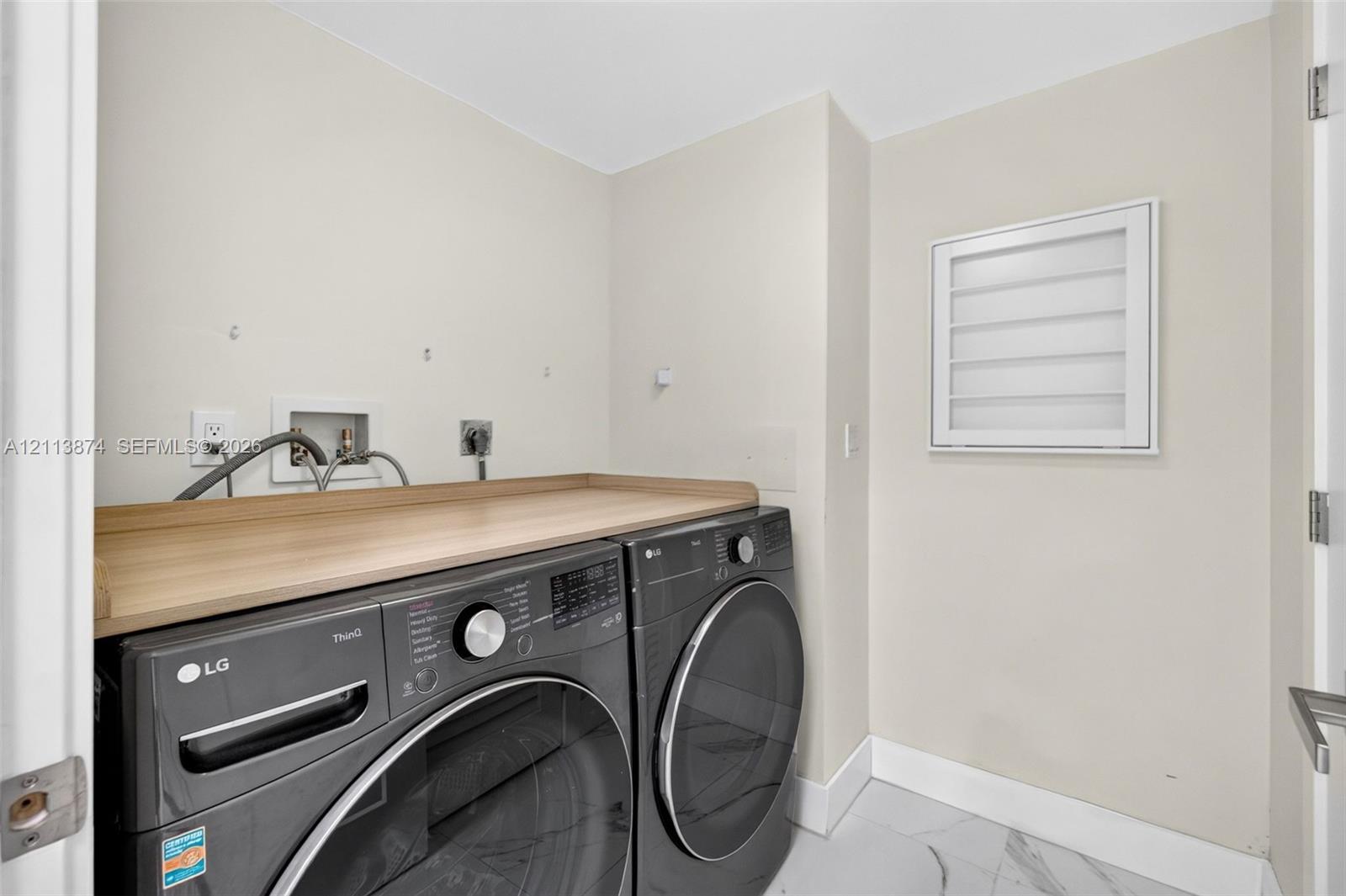 Dedicated laundry area featuring a wood-finish folding counter, tiled flooring, and a wall-mounted louvered shutter