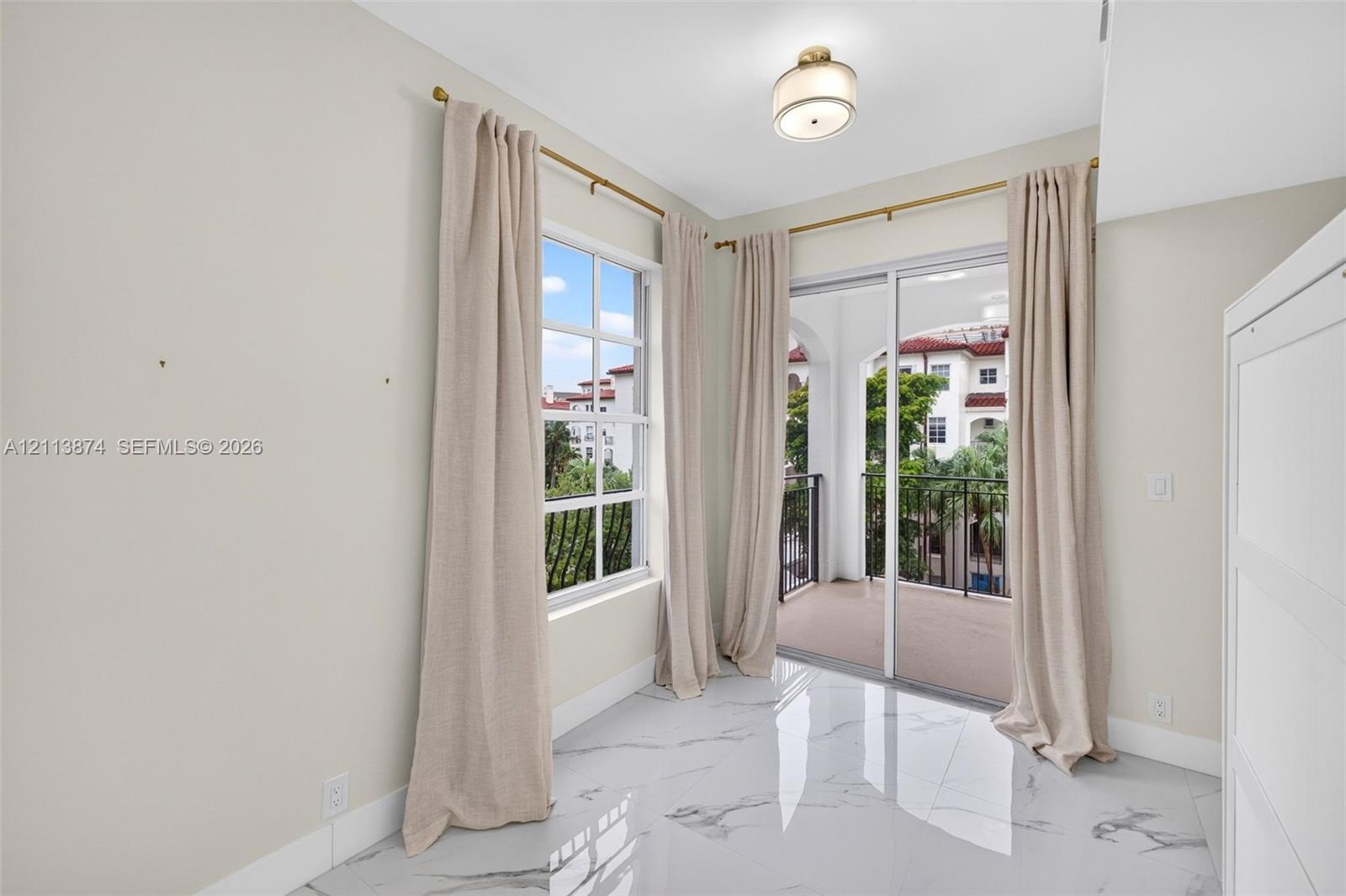 Large-format polished tile flooring, multi-pane window, flush-mount ceiling light, and sliding glass door with access to a covered balcony