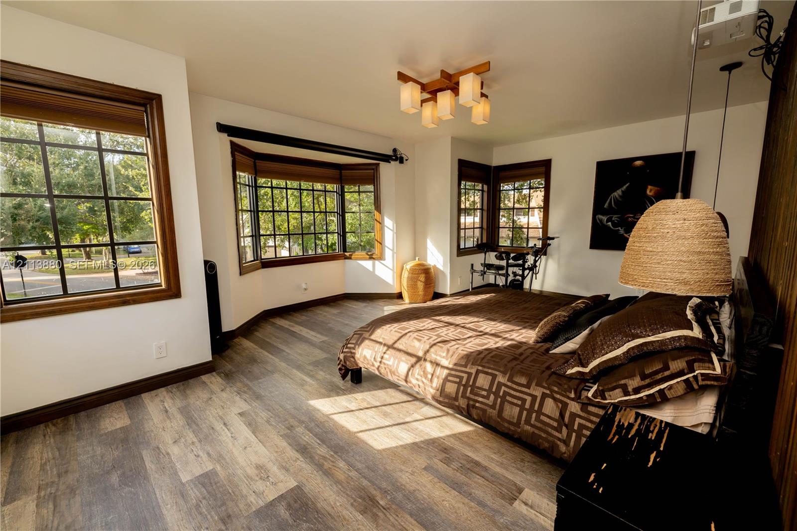 Wood-finish flooring, multi-pane windows with wood-tone casing, bay window, geometric-style multi-light ceiling fixture, and wood-paneled accent wall