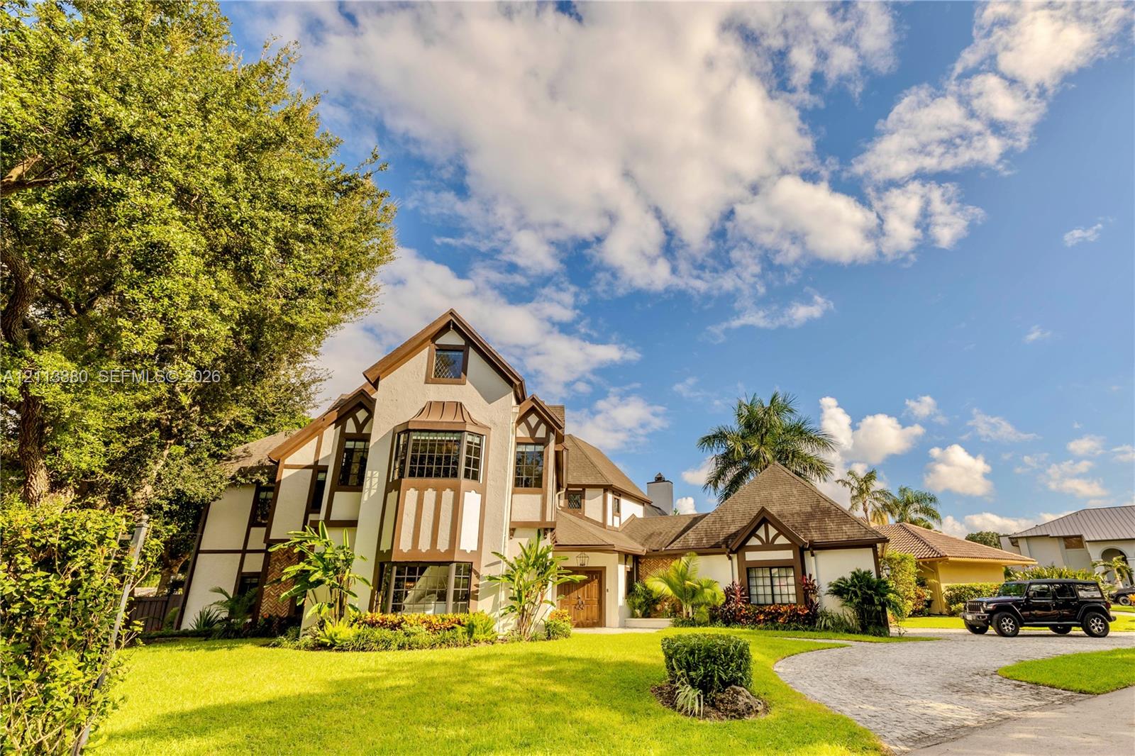 Tudor-style exterior featuring multi-gabled rooflines, decorative timber framing, a prominent multi-level bay window, and a gravel driveway