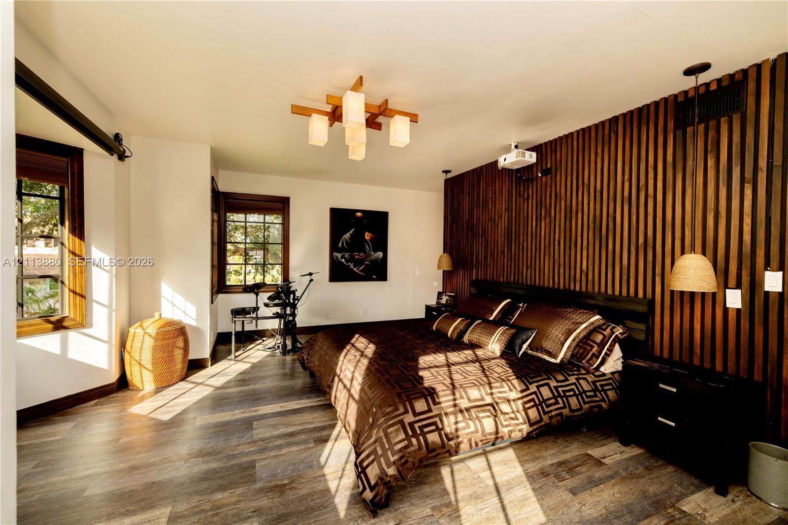 Interior space featuring a vertical wood-slat accent wall, wood-finish flooring, multi-pane windows with wood trim, a geometric multi-light chandelier, and integrated pendant lighting