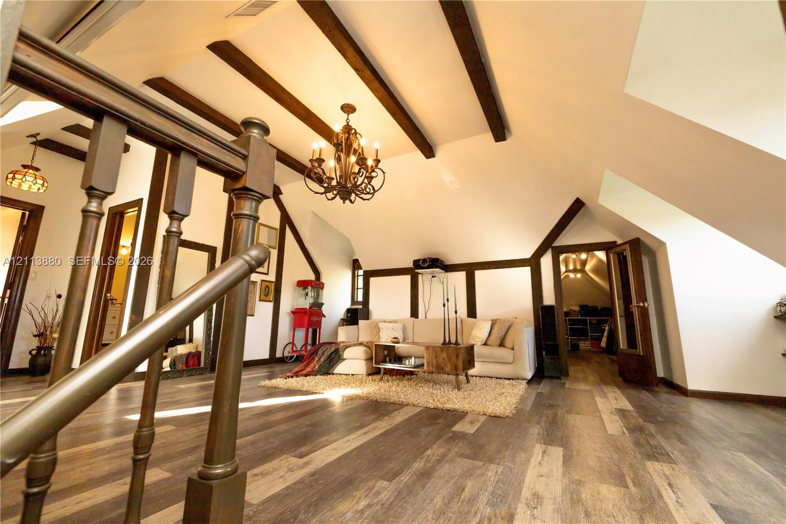 Vaulted ceiling featuring exposed dark wood beams, wood-finish flooring, decorative wood trim, and a multi-arm iron chandelier