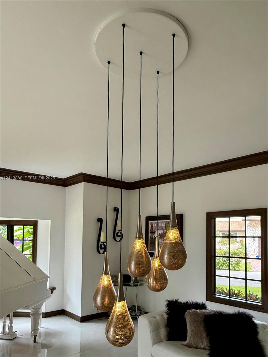 Multi-pendant light fixture featuring tiered metallic, teardrop-shaped shades, dark wood-finish window frames, and matching dark wood-finish crown molding