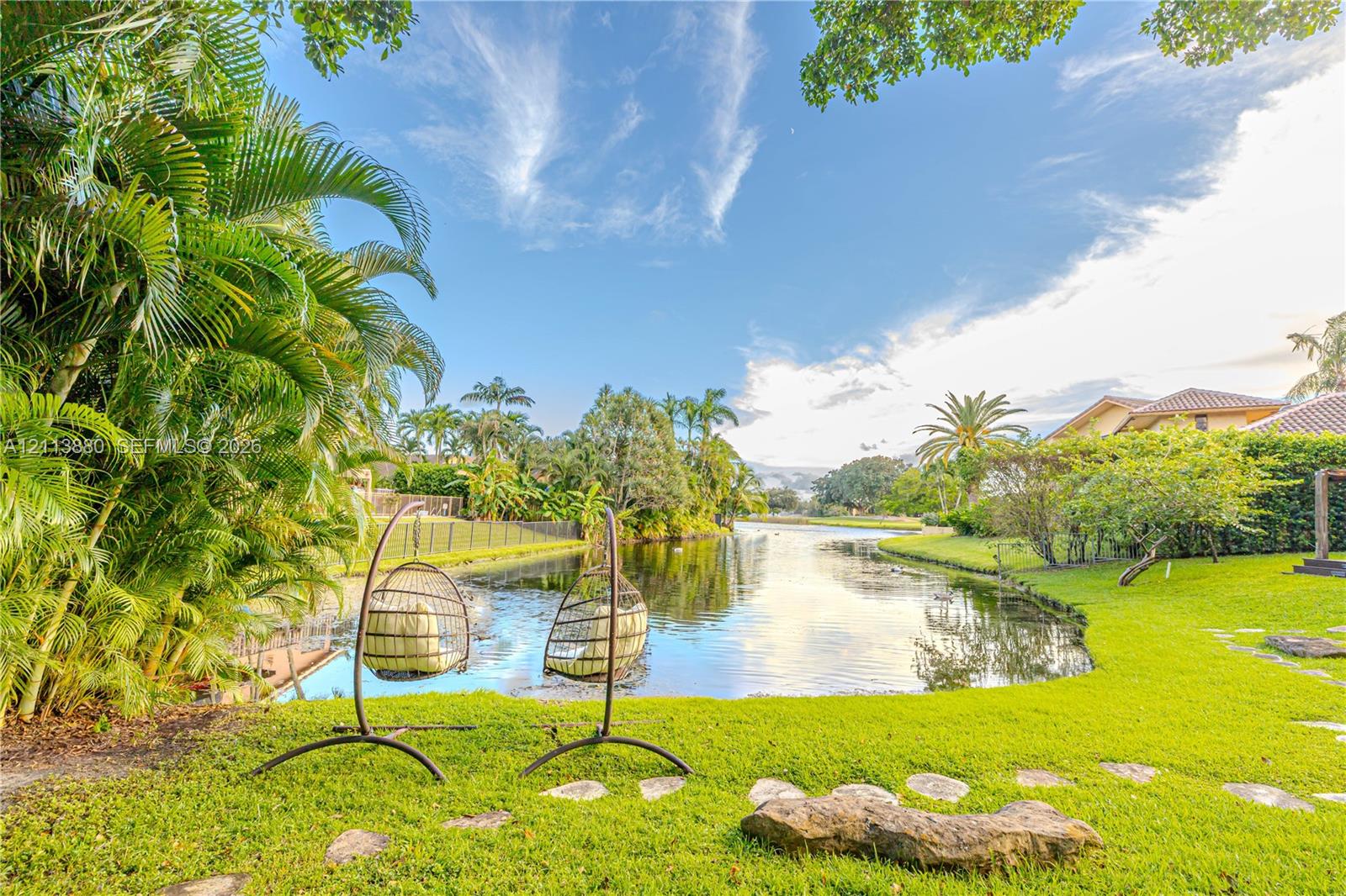 Waterfront backyard featuring a manicured lawn, established palm trees, and natural stone pathways