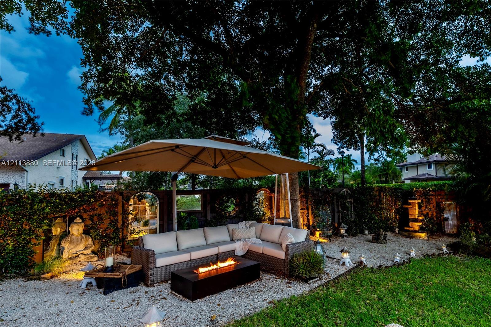 Backyard featuring a graveled lounge area, a stone-wall perimeter with integrated architectural mirror accents, mature tree canopy, and a tiered stone water feature