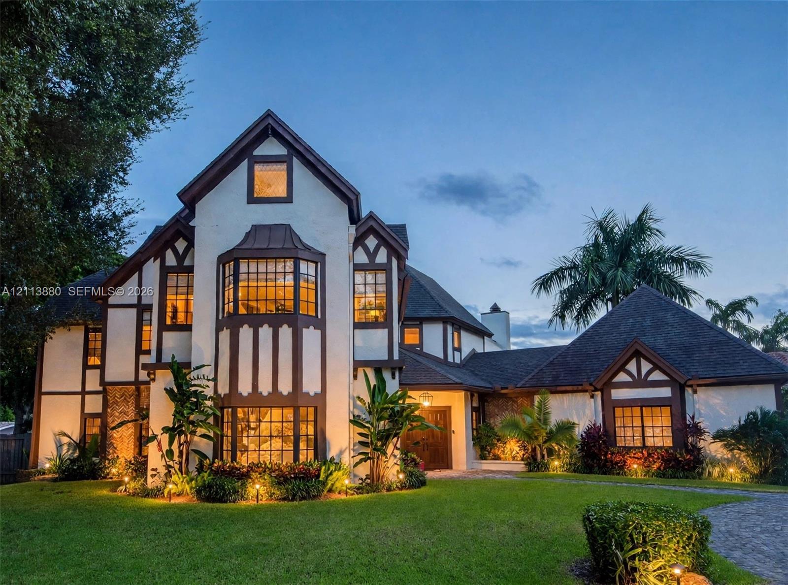 Tudor-style exterior featuring a multi-gabled roofline, decorative half-timbering, large bay windows, and a paved stone driveway Tudor-style exterior featuring a multi-gabled roofline, decorative half-timbering, large bay windows, and a paved stone driveway
